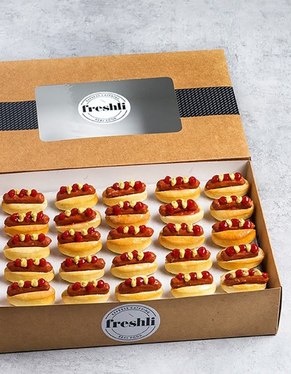 Box de 25 unidades de mini hot dogs con kétchup y mostaza.